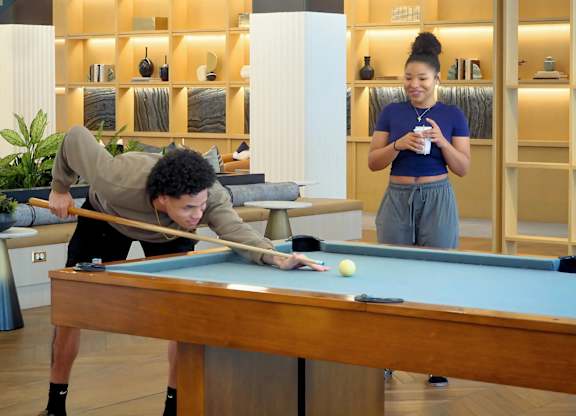 A man is playing pool while a woman watches and drinks coffee at Era Apartments in Denton, TX