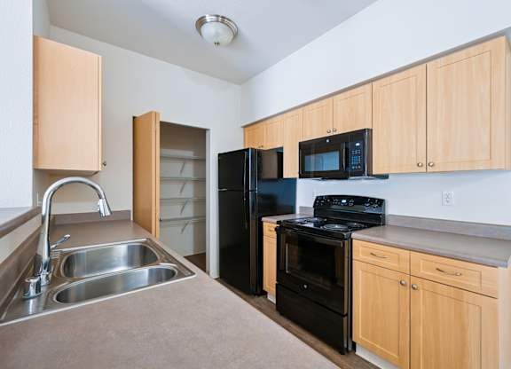 Soho kitchen with black appliances, a pantry closet, and wooden cabinets at Abbey Rowe Apartments in Olympia, WA