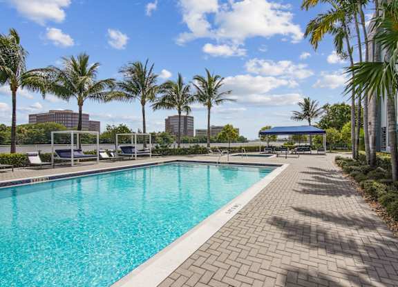 A sparkling swimming pool surrounded by palm trees and brick walkways at Blue Lagoon 7 Apartments in Miami, FL