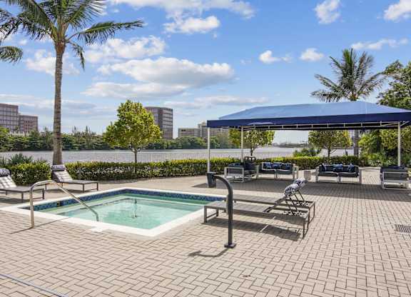 A hot tub with lounge chairs next to it and a shaded seating area in the background at Blue Lagoon 7 Apartments in Miami, FL