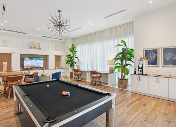 A pool table is in the middle of a clubroom with a TV, chairs, and coffee maker at Blue Lagoon 7 Apartments in Miami, FL