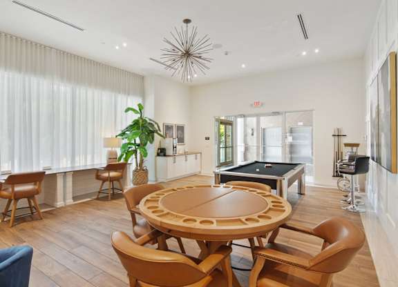 A clubroom with a round wooden table surrounded by chairs and a pool table in the background at Blue Lagoon 7 Apartments in Miami, FL