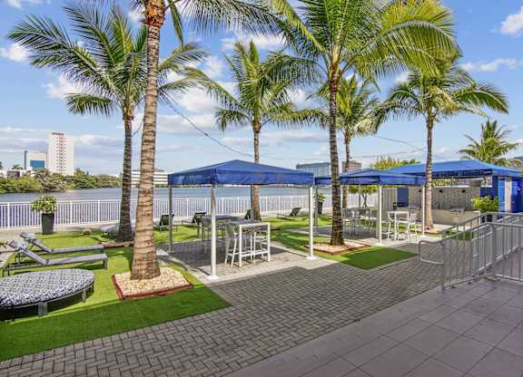 A sundeck area with palm trees and a blue canopies with seating at Blue Lagoon 7 Apartments in Miami, FL
