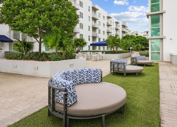 a seating area with tables and chairs on a lawn in front of an apartment building