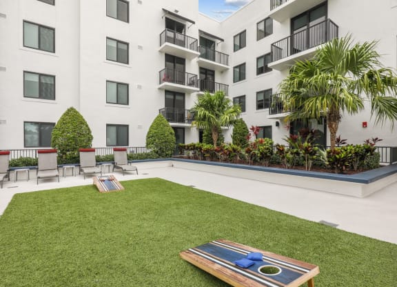 Courtyard area with cornhole boards in green space and chairs at Bay Village 1 in Palmetto Bay, FL