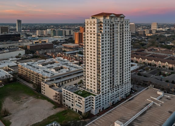 an aerial view of a tall building with a red roof and a parking lot in front of at Dominion Post Oak in Houston, TX