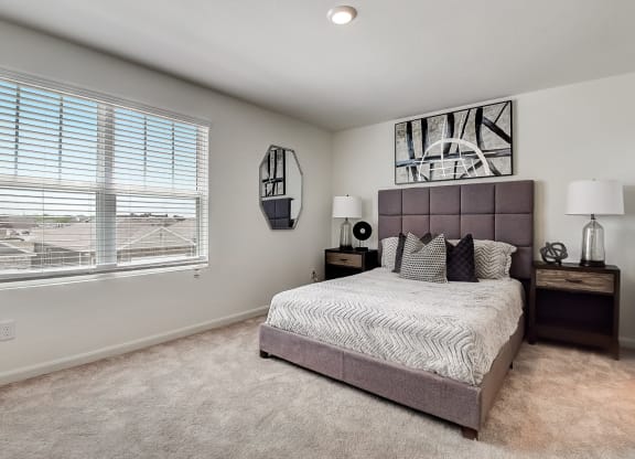 a model bedroom with carpet floor, big window and brown furnitures
