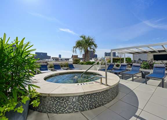 Rooftop pool with a hot tub with blue chairs and a white awning at Dominion Post Oak apartments in Houston, TX
