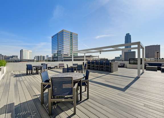 Wooden deck with chairs and a table with a metal frame on the rooftop patio at Dominion Post Oak apartments in Houston, TX