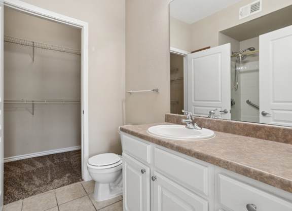 Edinburgh bathroom with a toilet, sink, and mirror at Encore at Buckingham Apartments in Richardson, TX