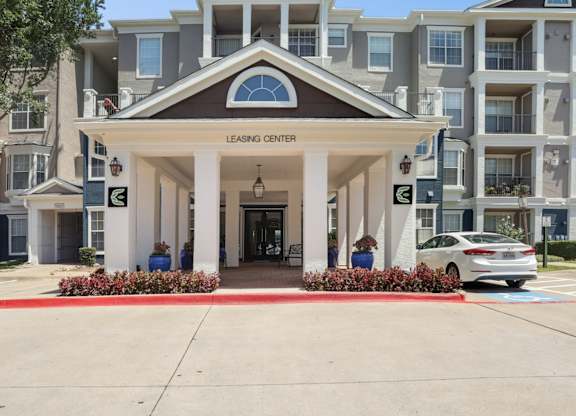 The entrance to the leasing office with white pillars and landscaping at Encore at Buckingham Apartments in Richardson, TX