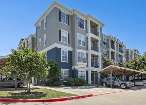 The exterior of the apartment complex with a parking lot in front at Encore at Buckingham Apartments in Richardson, TX