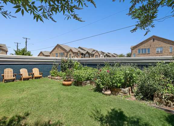 A lush garden with chairs and apartment buildings in the background at Encore at Buckingham Apartments in Richardson, TX