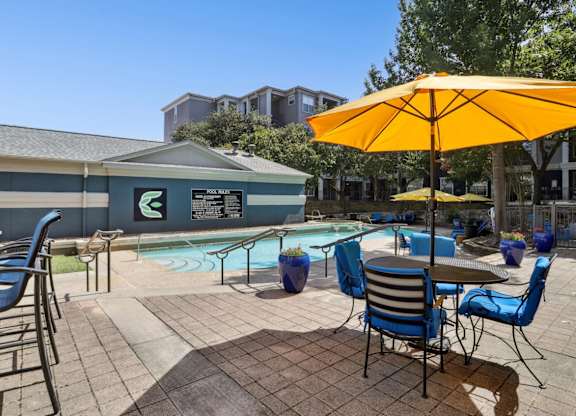 A pool area with chairs and a yellow umbrella at Encore at Buckingham Apartments in Richardson, TX