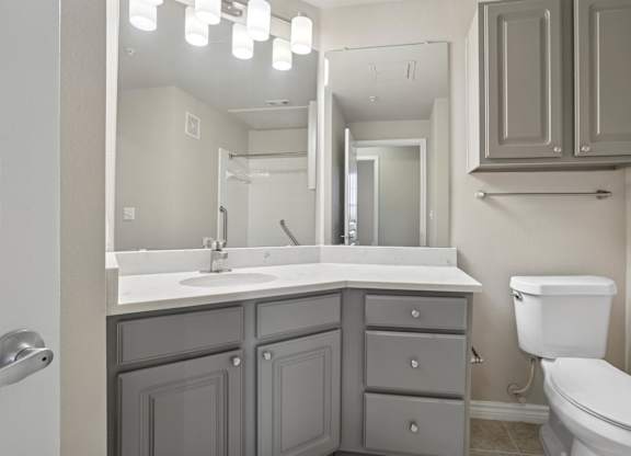 Kenzington bathroom with a white toilet and a sink with a mirror above it at Encore at Buckingham Apartments in Richardson, TX