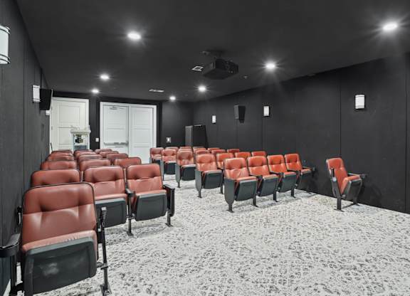 A movie theater with black walls and red seats at Encore at Buckingham Apartments in Richardson, TX