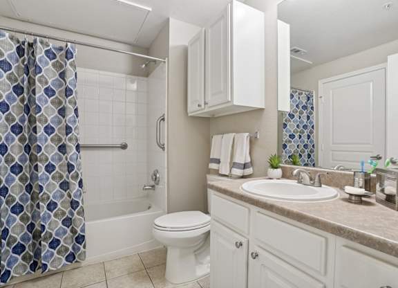 Windsor bathroom with a white toilet and a shower curtain and a sink at Encore at Buckingham Apartments in Richardson, TX