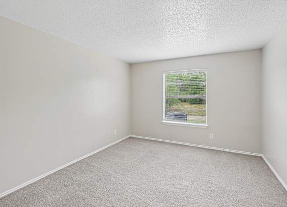 A room with a window showing a view of a road and trees.