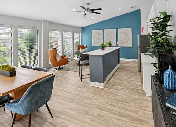 A modern clubhouse with comfortable seating, a ceiling fan, kitchen, and wood floors at Estelle Creek North Apartments in Irving, TX