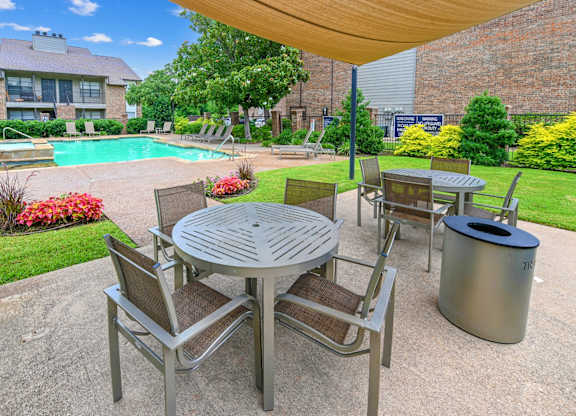 A patio with a table and chairs is surrounded by a pool and a brick building.