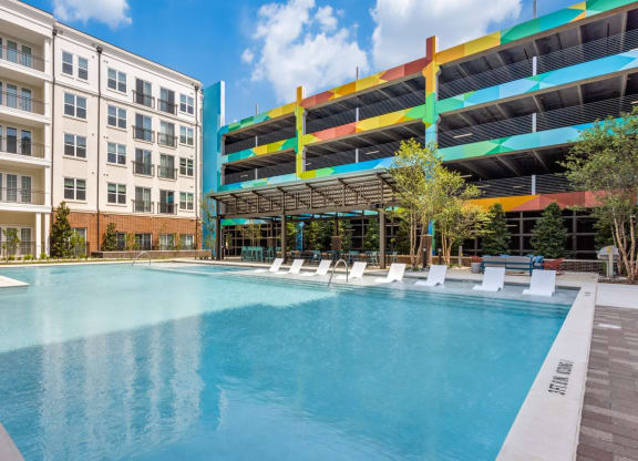 Resort-style swimming pool with in-pool white lounge chairs and parking garage in background at Era Apartments in Denton, TX