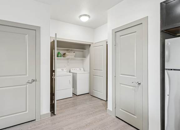 A dedicated laundry space with a full size washer and dryers and shelves at GreenVue Apartments in Richardson, TX