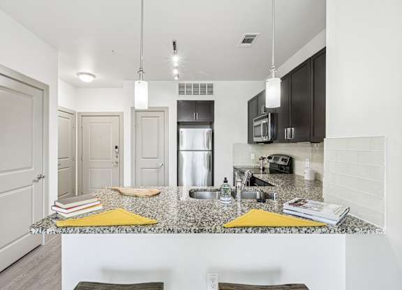 A kitchen with a granite countertop and dark cabinets at GreenVue Apartments in Richardson, TX