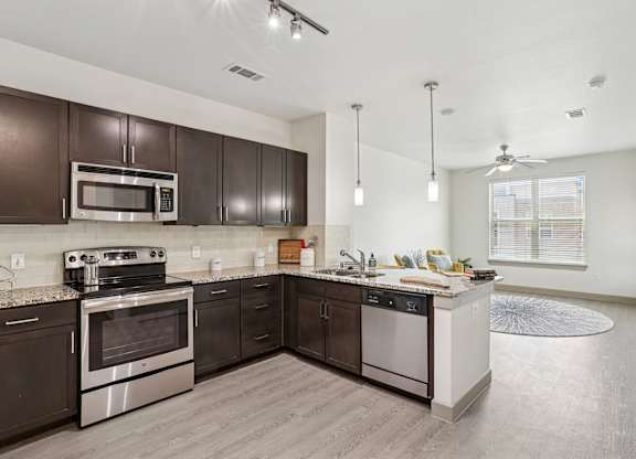 A modern kitchen with dark brown cabinets and stainless steel appliances at GreenVue Apartments in Richardson, TX