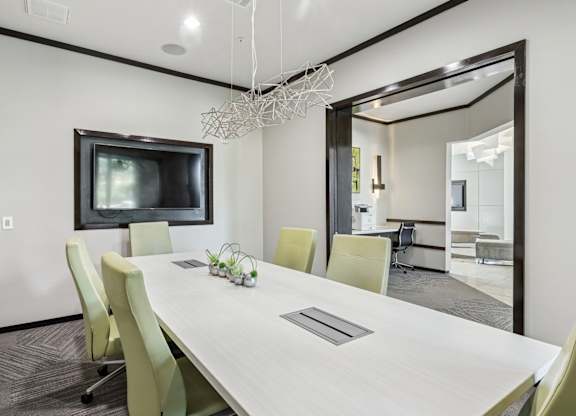 A modern conference room with a long table, chairs, and a television at GreenVue Apartments in Richardson, TX
