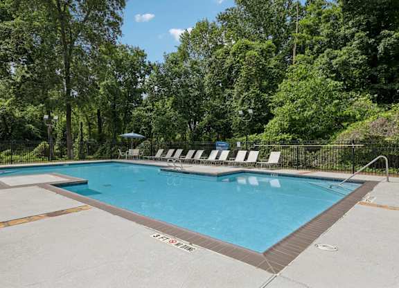 A pool with lounge chairs surrounded by lush trees at Gwinnett Square Apartments in Duluth, GA