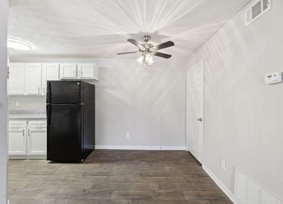 A black fridge in the kitchen leading to a dining area with a ceiling fan at Gwinnett Square Apartments in Duluth, GA