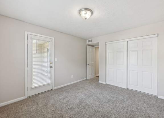 A bedroom with a carpeted floor, closet, and glass door leading to a balcony at Gwinnett Square Apartments in Duluth, GA