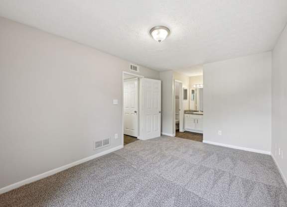 A bedroom with carpet leading to a bathroom and closet  at Gwinnett Square Apartments in Duluth, GA