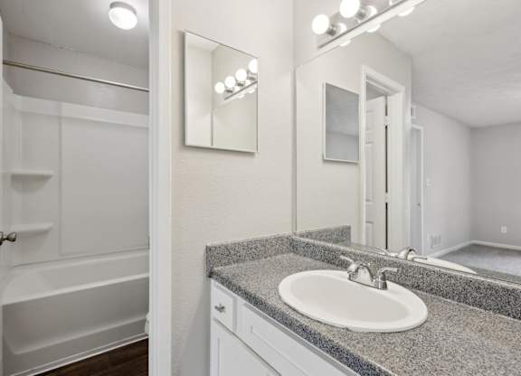 A bathroom with a sink, mirror, and a bathtub at Gwinnett Square Apartments in Duluth, GA