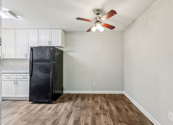 A black refrigerator is in a kitchen and dining area with white cabinets at Gwinnett Square Apartments in Duluth, GA