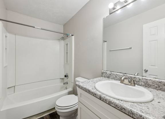 A white bathroom with a toilet, sink, mirror, and bathtub at Gwinnett Square Apartments in Duluth, GA