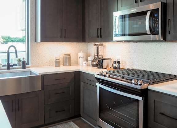 3 bedroom model kitchen with stainless steel appliances, quartz countertops, and a window at The Hamilton apartments in Dallas, TX