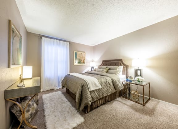 Model bedroom with large bed and dresser at Hillside Creek Apartments in Austin, TX