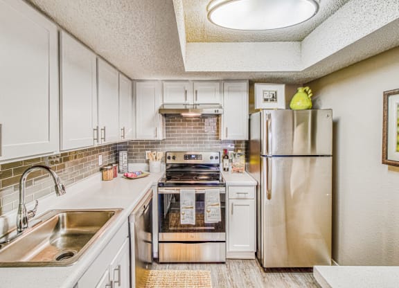 Model home renovated kitchen with stainless steel appliances and white cabinets at Hillside Creek Apartments in Austin, TX