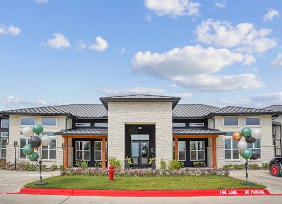 A leasing office exterior with lush grass, flowers, and welcoming balloons at Hillside on Parmer Lane Apartments in Austin, TX