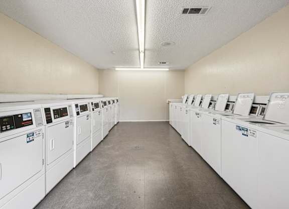 An onsite laundry center holds a row of washing machines and a row of dryers at Heritage Square Apartments in Waco, TX