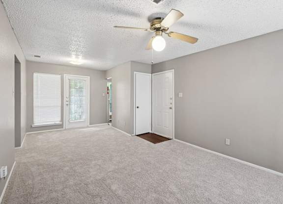 A living room with a ceiling fan and carpeted floor at Heritage Square Apartments in Waco, TX