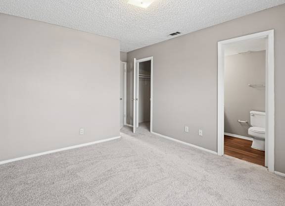 A bedroom with a carpeted floor and a door to the bathroom at Heritage Square Apartments in Waco, TX