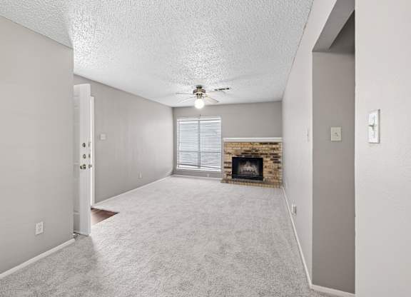 A spacious living room with a brick fireplace and a ceiling fan at Heritage Square Apartments in Waco, TX