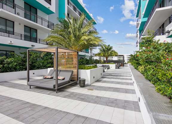 Cushioned lounge chair next to a palm tree in ou courtyard at Hollywood Heights on the Boulevard Luxury Apartments in Hollywood FL