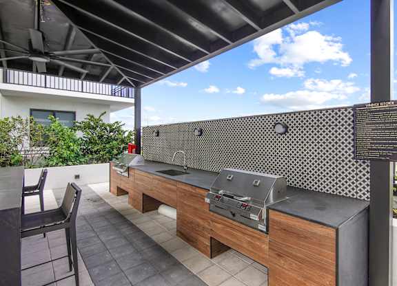 Outdoor grilling station with two BBQ grills, a sink, and ample seating under a pergola  Balcony view of Hollywood Boulevard at Hollywood Heights on the Boulevard Luxury Apartments in Hollywood, FL