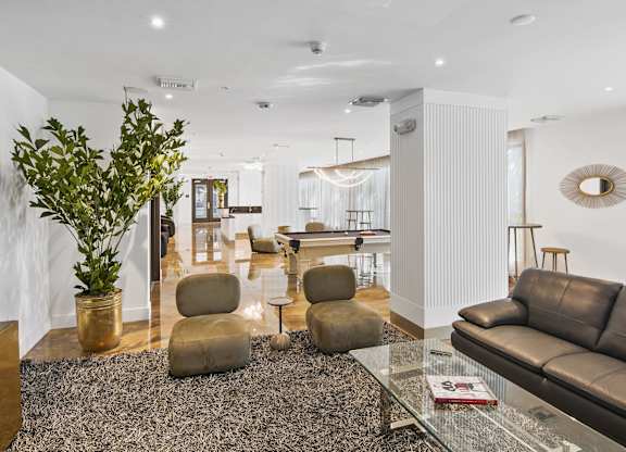 lounge area with brown chairs, a grey couch, and a green plant with our social club with a pool table in the background at Hollywood Heights on the Boulevard Luxury Apartments in Hollywood FL