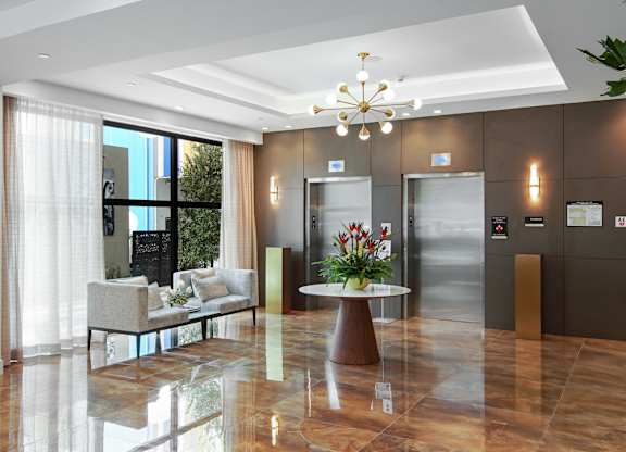 Lobby area with white table with a flower arrangement, white chairs and elevators at Hollywood Heights on the Boulevard Luxury Apartments in Hollywood, FL