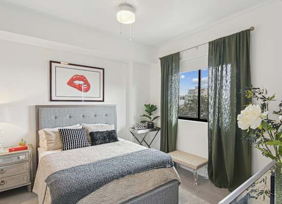 A bedroom with a large bed and a framed picture of red lips above it and a window with green curtains at Hollywood Heights on the Boulevard Luxury Apartments in Hollywood, FL