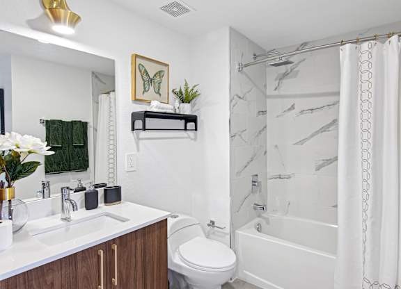 A bathroom with a marble shower, a white counter with wooden cabinets and a white toilet at Hollywood Heights on the Boulevard Luxury Apartments in Hollywood, FL